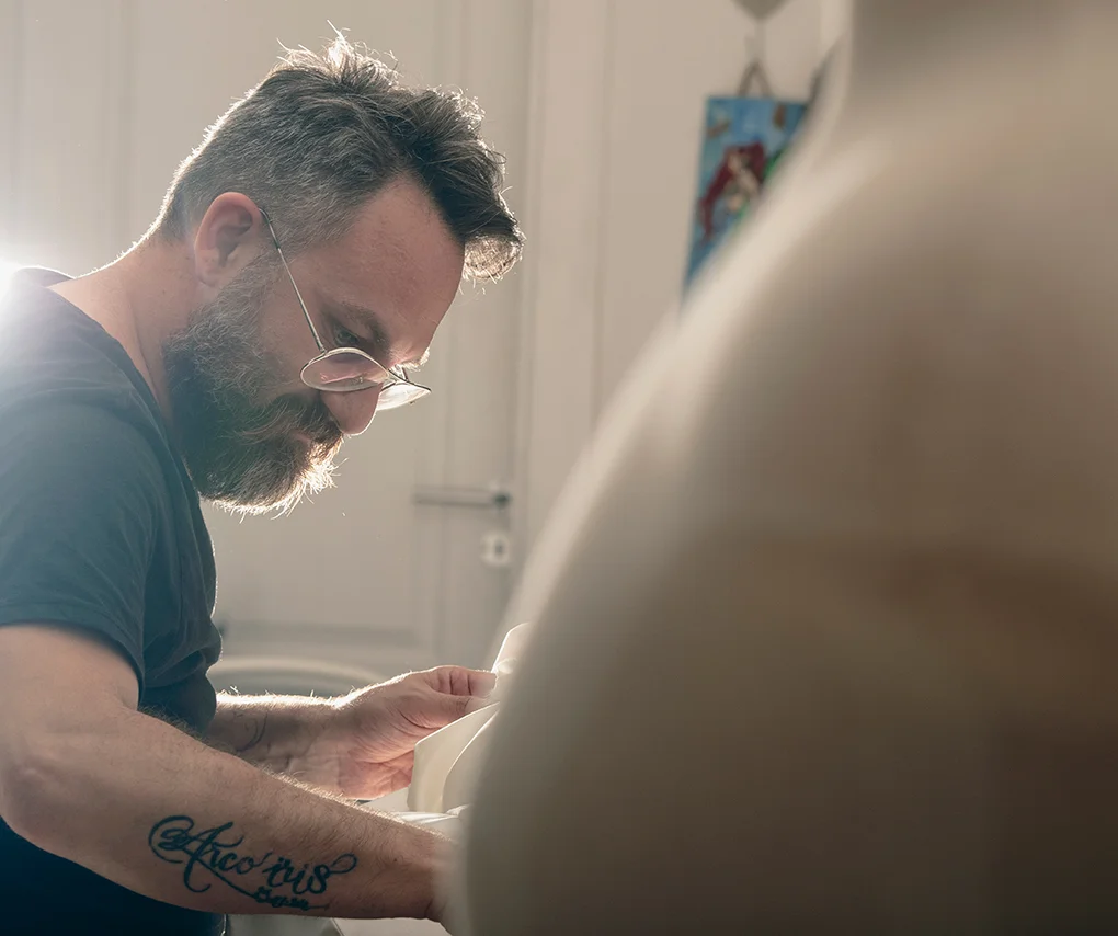Hombre con tatuaje cosiendo tela blanca en taller de costura - Gianluca Urraso