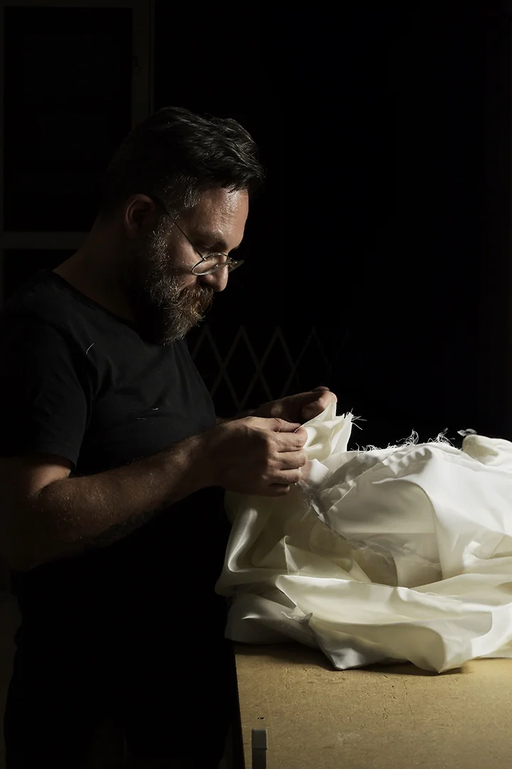 Hombre con gafas cosiendo tela blanca - Gianluca Urraso