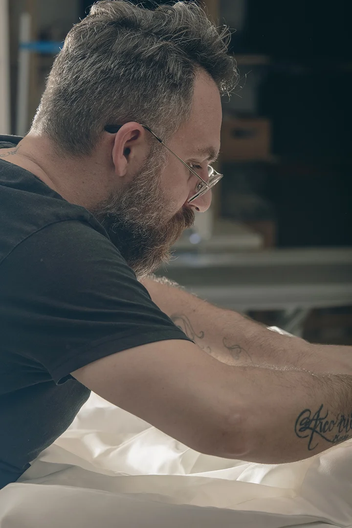 Hombre con barba y gafas trabajando en tela blanca. - Gianluca Urraso