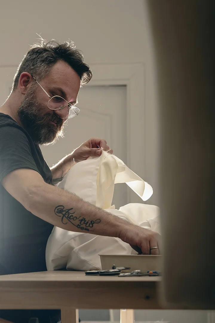 Hombre con tatuaje cosiendo tela blanca en taller de costura - Gianluca Urraso